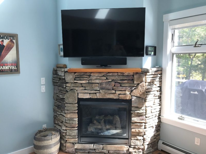 Tv mounted over stonework fireplace in modern home living room with soundbar.