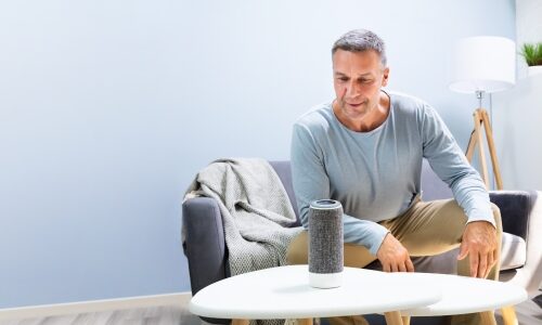 An older individual using a voice assistant as an example of an aging in place technology.