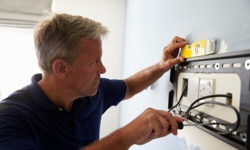 Man mounting flat-panel TV bracket on wall.