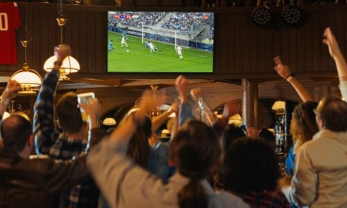 Bar patrons cheering at broadcast TV, representation of medium and audience affected by Next Gen TV atsc 3.0 standard