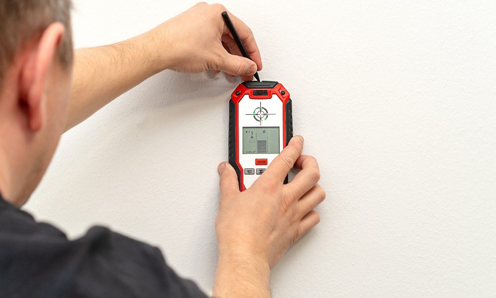 Man using a stud-finder to find studs in a piece of drywall.