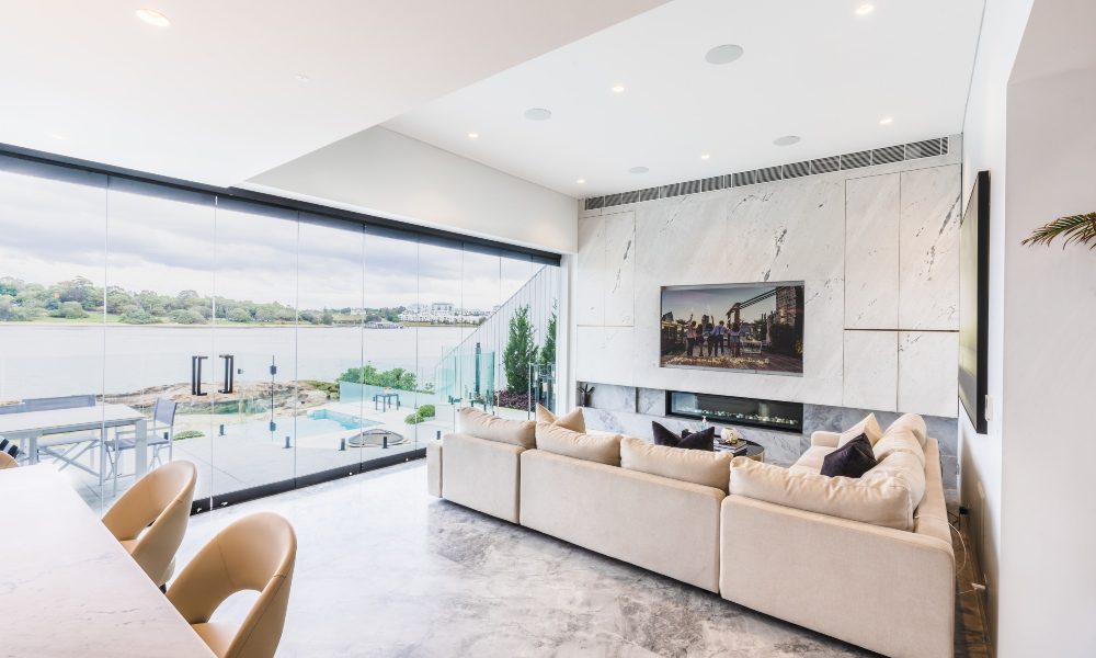 Living area with television mounted onto white marble wall over the fireplace and open-air patio overlooking Gladesville bay.