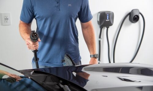 Man standing at electric car with Legrand Level 2 Plug-In EV charger at the ready in residential garage.