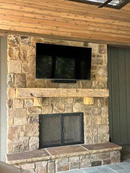 Outdoor TV and soundbar set-up over rustic fireplace in outdoor entertainment system Mozaic Integrated Technology Design