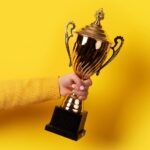 Woman holding award trophy out symbolizing the ceremony used to congratulate Home of the Year Award winners