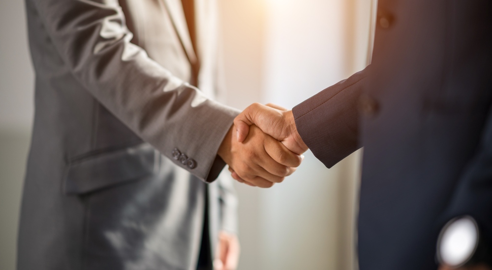 Two businessmen shaking hands to symbolize ECNY joining AHT Global