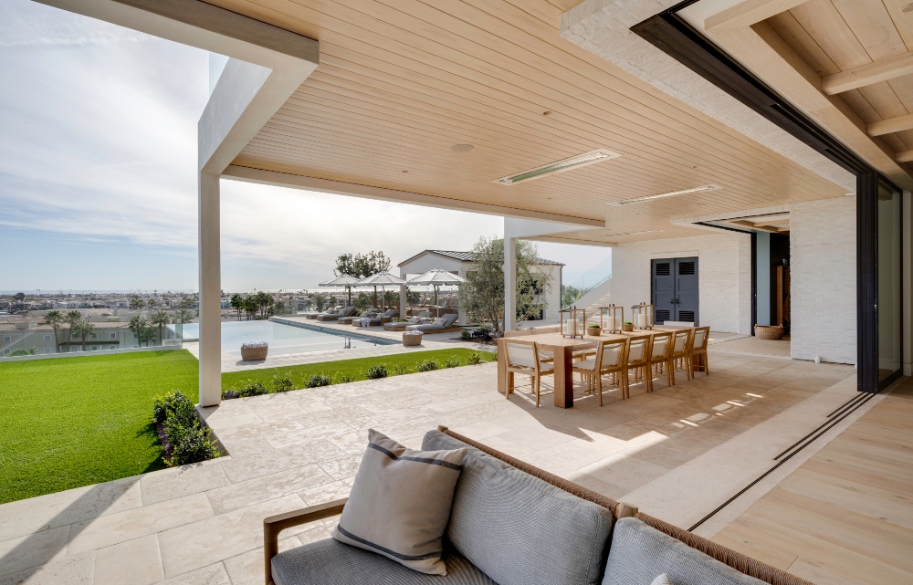 A spacious outdoor dining area with a large table and chairs, overlooking a pool and green lawn.