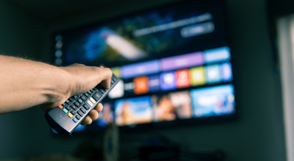 Man watching a streaming service provider through a TV meant to symbolize viewership numbers discussed in the most recent Nielsen The Gauge report
