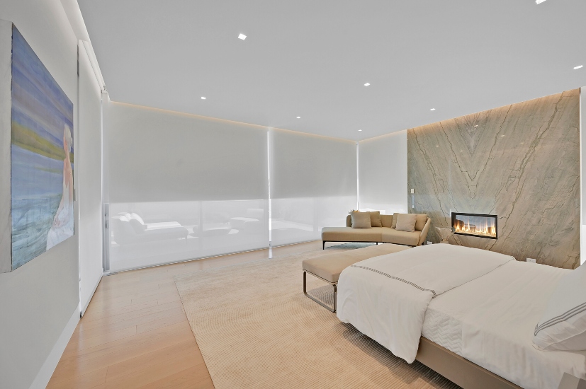 Sophisticated master suite of luxury Florida mansion surrounded by floor-to-ceiling windows with dual window treatments—solar and blackout shades—concealed for clean aesthetics.
