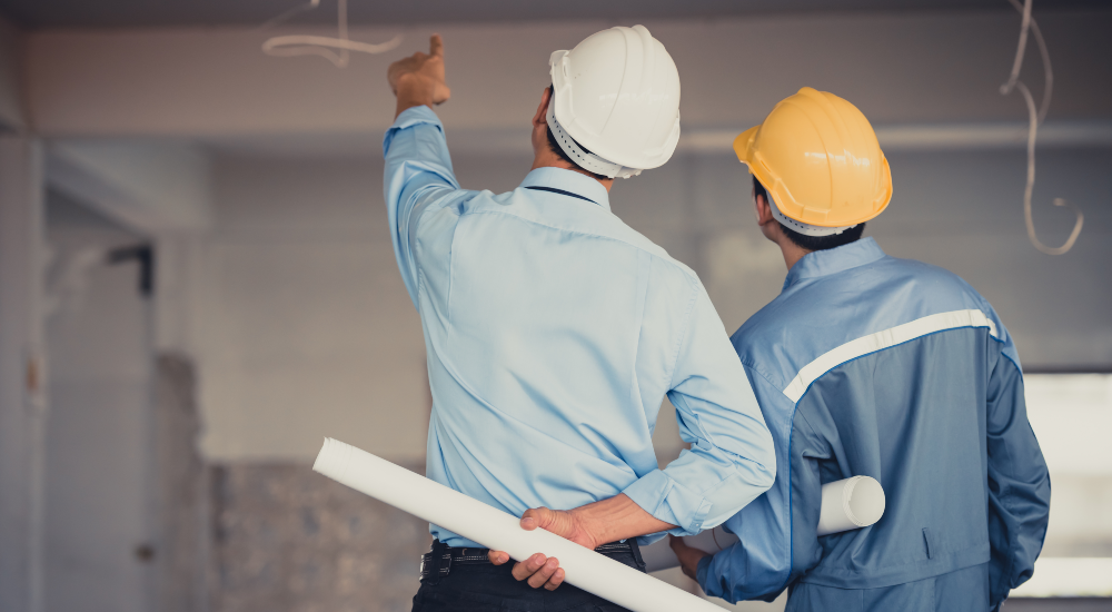 Two contractors standing in the middle of an unfinished room discussing remodel plans concept representing luxury home market conditions