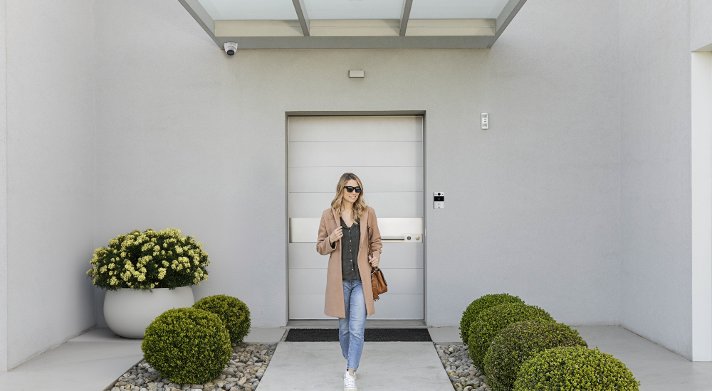 Woman walking out of home with smart doorbell and security camera in shot as an example of a smart lifestyle enabled by Yubii OS from Nice