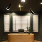 Dark olive drenched modern office with honey-colored oval desk behind light filtering shades in Lutherville, Maryland.