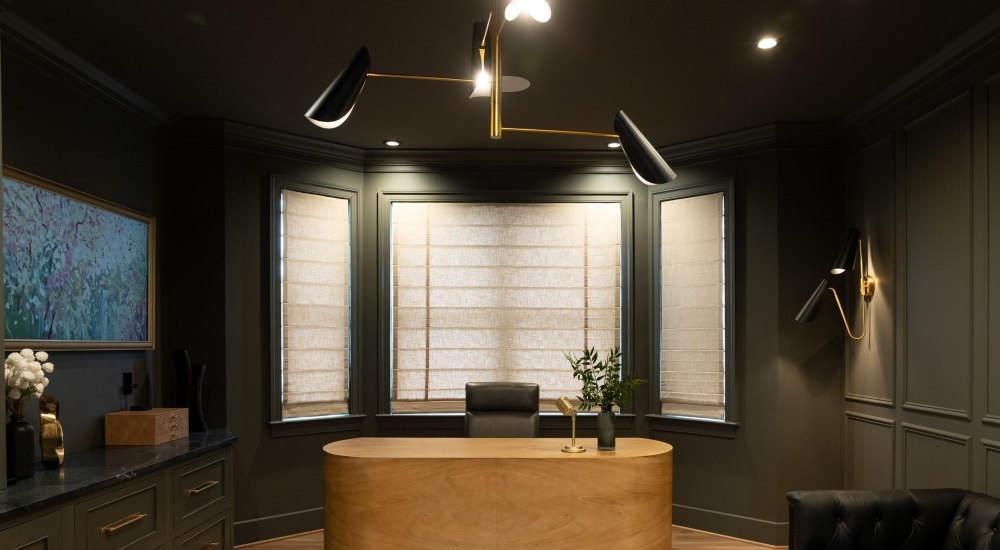 Dark olive drenched modern office with honey-colored oval desk behind light filtering shades in Lutherville, Maryland.