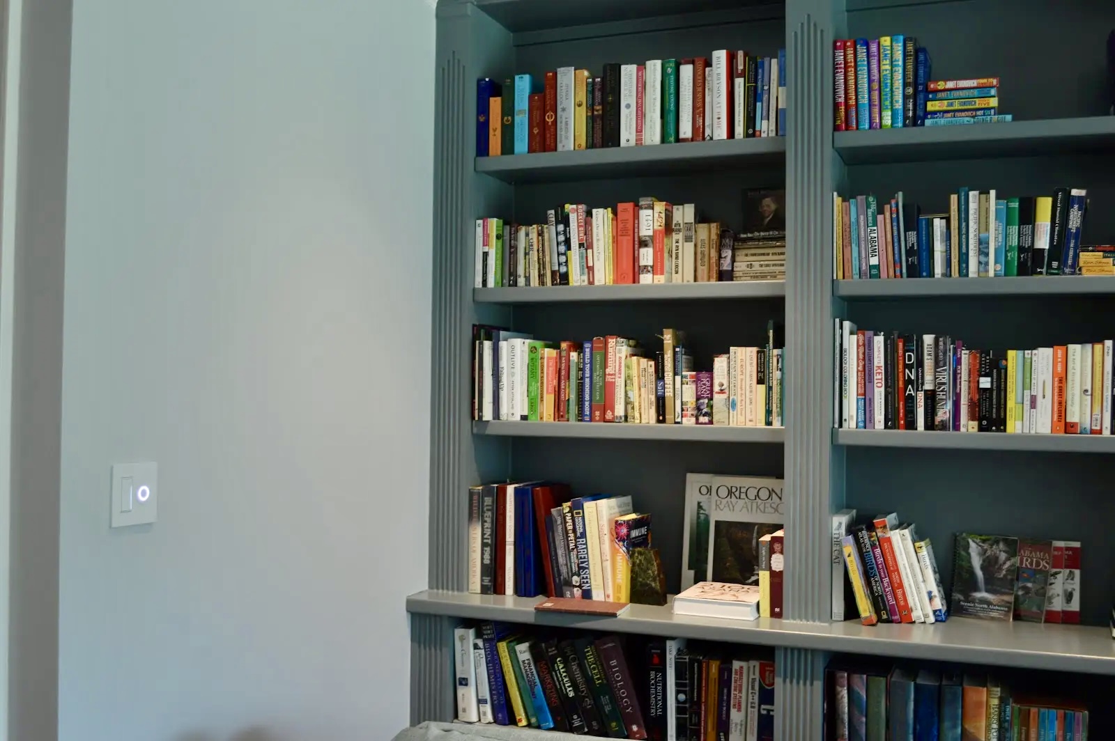 A wall-mounted touchscreen control interface installed beside a bookshelf, offering the homeowner intuitive access to the whole-home audio system.